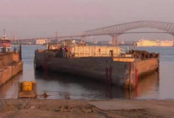前文提到的猎户座号潜艇母舰的“独木舟”离开拆解码头的画面。黄色的牵引头之后会将其拖上海滩。